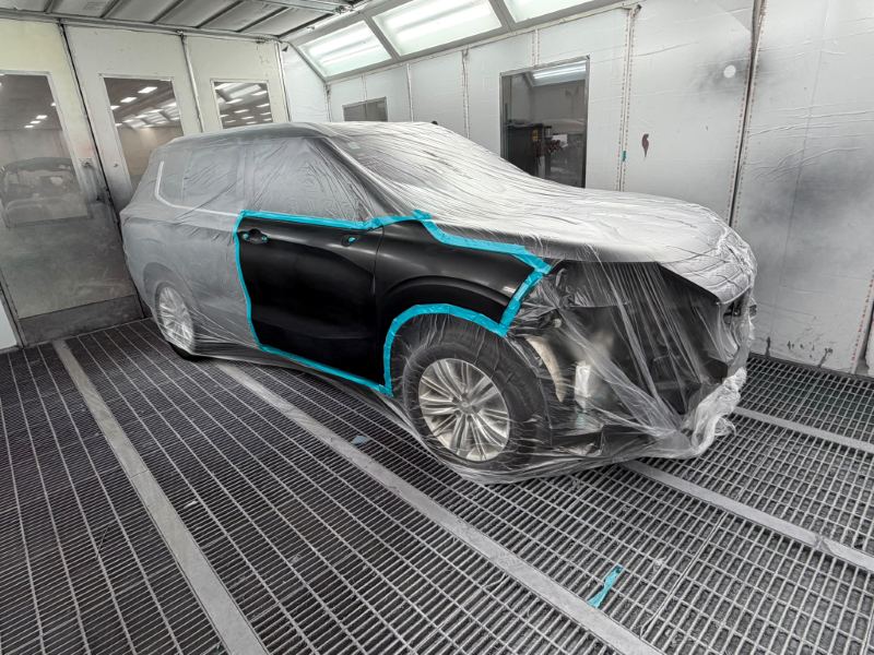 Black Mitsubishi SUV masked in the spray booth with its front door and guard painted